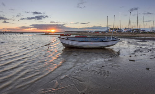 Sailboats moored on beach against sky during sunset