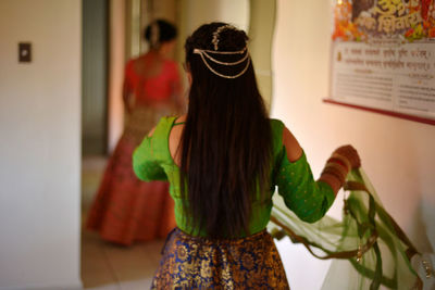 Rear view of woman in sari standing by wall at home