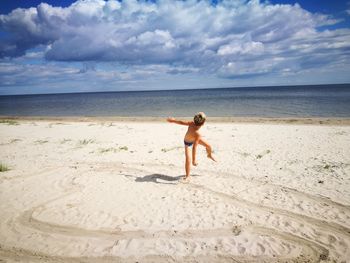 Full length of shirtless boy playing on beach against sky