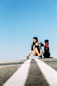 Woman with dog and skateboard against clear blue sky