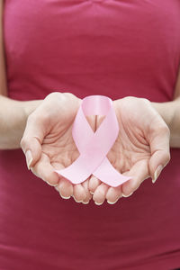 Midsection of woman holding pink ribbon