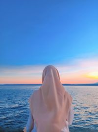 Rear view of woman looking at sea against sky during sunset