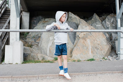 Boy standing against a pole looking out at the track in sports clothes