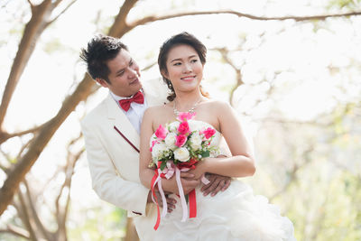 Newlywed couple holding flower bouquet outdoors