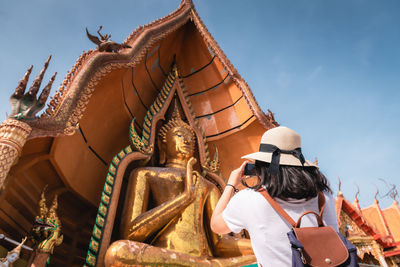 Low angle view of woman clicking photograph against temple building during sunny day