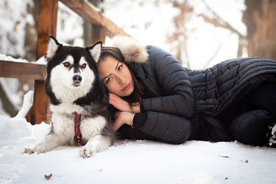 Portrait of woman with dog lying down on snow covered land