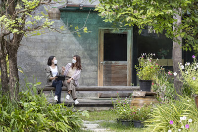 Two business women talk to each other in a shady cafe garden where masks are worn all the time.