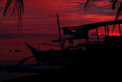 Silhouette of fishing boat in sea during sunset