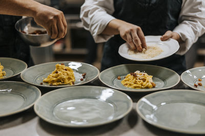 Female and male chef garnishing pasta on plate at kitchen counter in restaurant