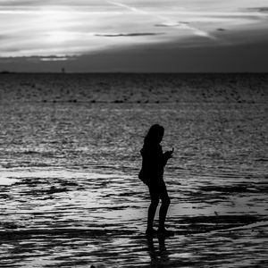 Silhouette woman standing on beach against sky during sunset