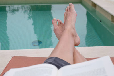 Low section of woman reading book in swimming pool