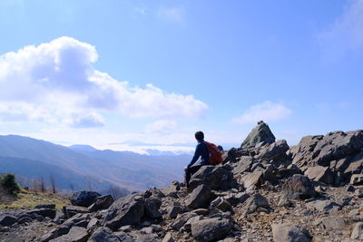 Rear view of man sitting on rock against sky