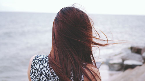 Rear view of woman standing at beach against sky