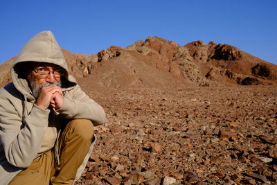 Side view of senior man sitting on rock against clear sky
