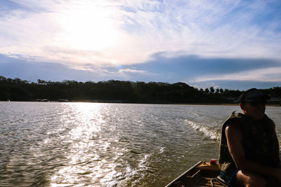 Rear view of man sitting on lake against sky