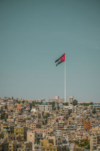 Flag against buildings in city against clear blue sky