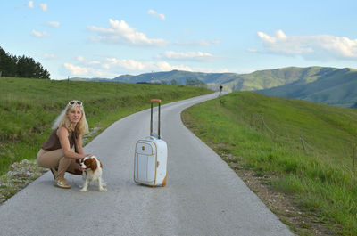 Woman and her dog, with suitcase on a mountain road in late afternoon