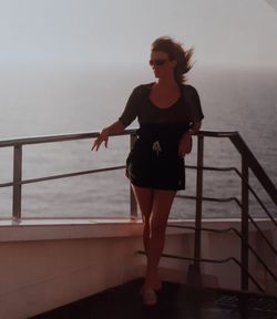 Full length of woman standing by railing against sea