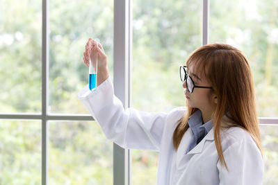 Teenage girl examining chemical in test tube against window