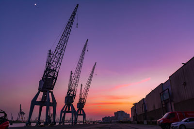 Cranes at construction site against sky during sunset