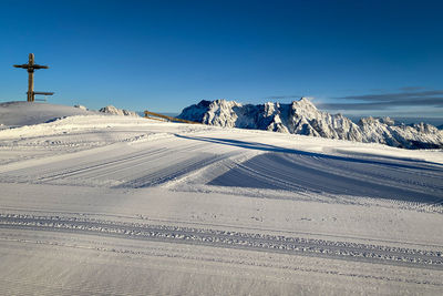 Scenic view of snow covered leogang mountains with summit cross of wildenkarkogel against blue sky