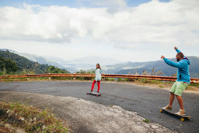 Couple skateboarding on road against sky