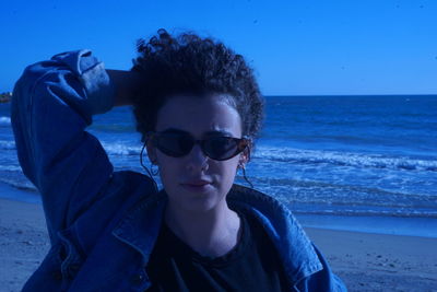 Portrait of beautiful woman wearing sunglasses at beach against sky