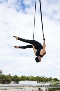 Low angle of fit male gymnast hanging on aerial straps during training in park