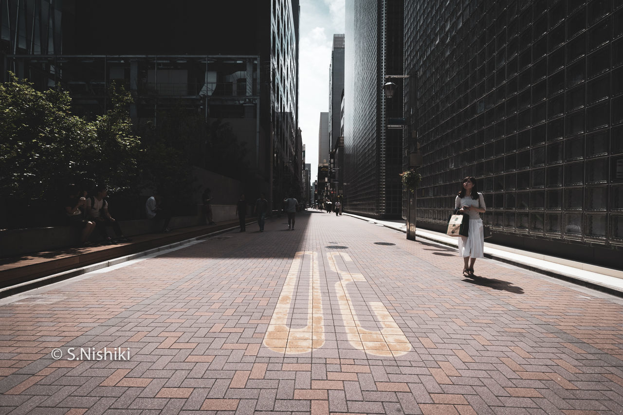 MAN WALKING ON FOOTPATH AMIDST CITY