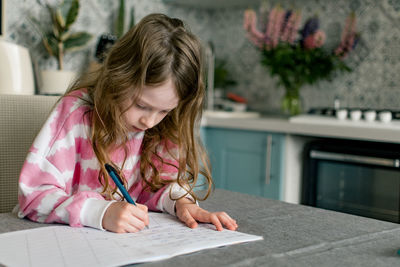 School girl going homework at home, writing in notebook.