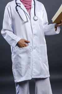 Midsection of doctor reading book while standing against gray background