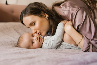 Satisfied mother kisses her sweet baby on the bed