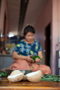 Close-up of coconut on cutting board with woman in background at home