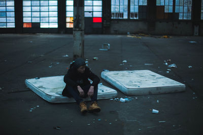 Man sitting on dirty mattress at weathered building