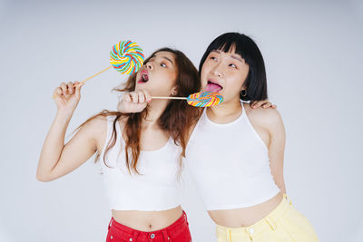 Lesbian couple holding lollipop against white background