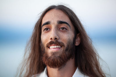 Smiling bearded young man with long brown hair looking away