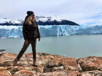 Mature woman wearing warm clothing while standing on rock by sea during winter