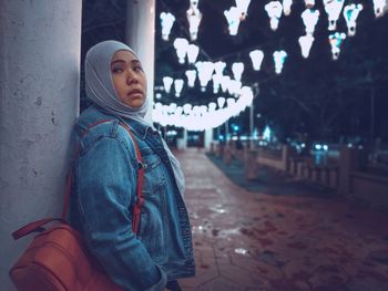 Woman looking away while standing in city at night
