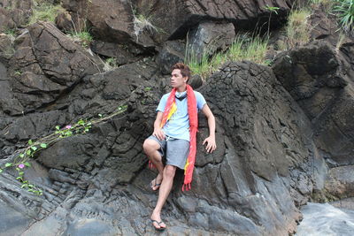 Young man looking away while leaning on rock