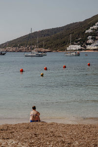 Woman sitting alone on beach by sea against clear sky in ibiza, spain