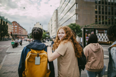Portrait of happy teenage girl looking over shoulder while walking with friends in city street