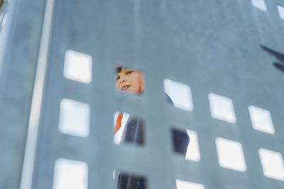 Low view of young boy through metallic fence while smiling to camera