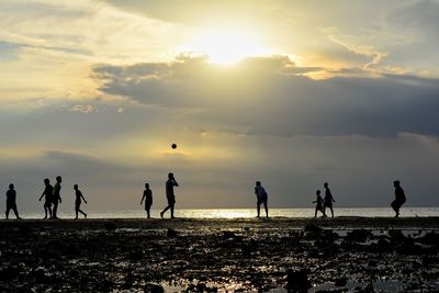 Silhouette people playing at beach against sky during sunset