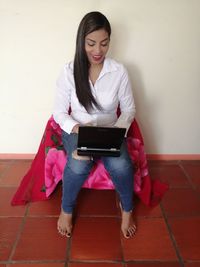 Young woman using phone while standing on wall