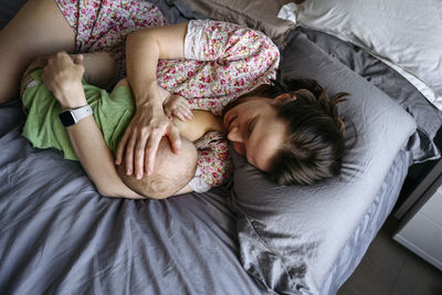 Mother breastfeeding boy lying on bed at home