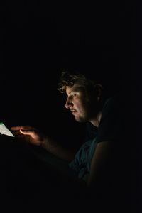 Side view of young man sitting in the dark