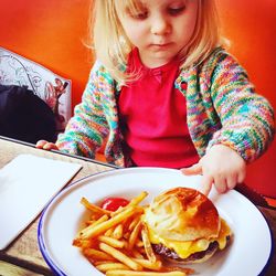 Close-up of cute girl touching burger served in plate with french fries at table