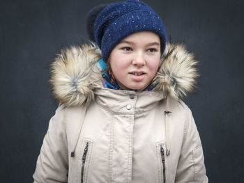 Close-up of girl wearing knit hat and fur coat during winter by wall