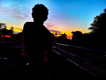 Silhouette man standing by railing against sky during sunset