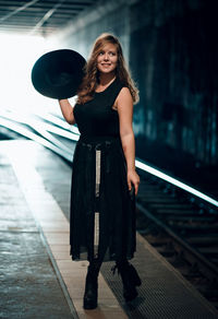 Full length of woman holding hat standing on railroad station platform